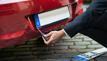 Man Placing New Empty White Number Plate On His Red Car