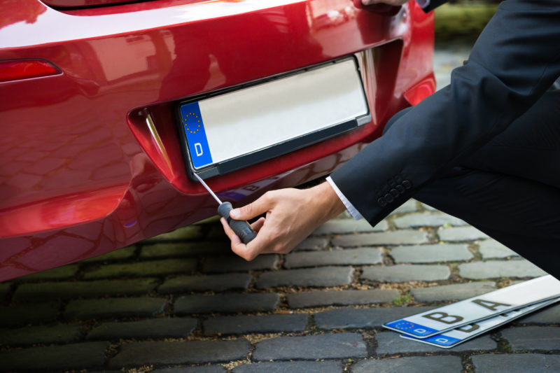 Man Placing New Empty White Number Plate On His Red Car