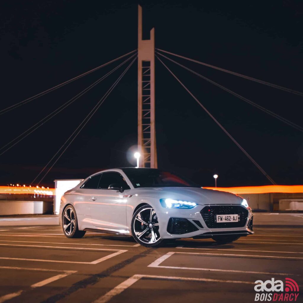 Audi RS5 Milltek grise de nuit, devant un pont éclairé