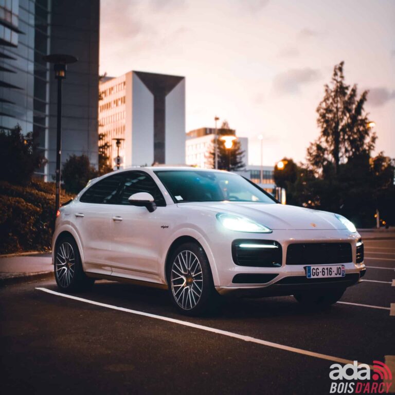 Porsche Cayenne Coupé blanc devant des immeubles de bureaux modernes, pour un déplacement professionnel depuis les Hauts-de-Seine